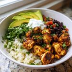 Close-up of a vibrant chicken burrito bowl featuring seasoned chicken, rice, black beans, avocado, and sour cream.