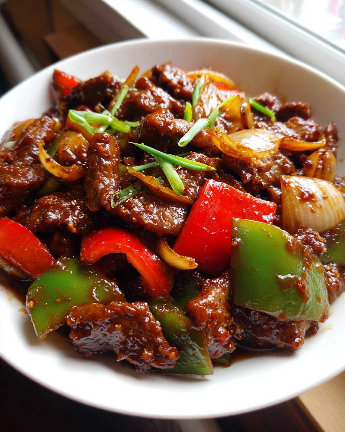 A close-up shot of glossy, saucy chinese pepper steak mixed with bright red and green bell peppers and onions.
