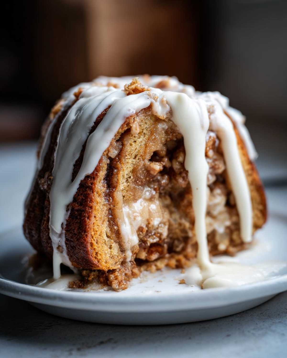 A close-up of a portion of cinnamon roll apple pie, rich with filling and drizzled heavily with white cream cheese icing.