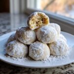 A stack of delicious cinnamon sugar snowball cookies heavily dusted with powdered sugar, one cookie is broken open.