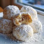 A stack of five powdered sugar-dusted cinnamon sugar snowball cookies, one broken open to show the texture.