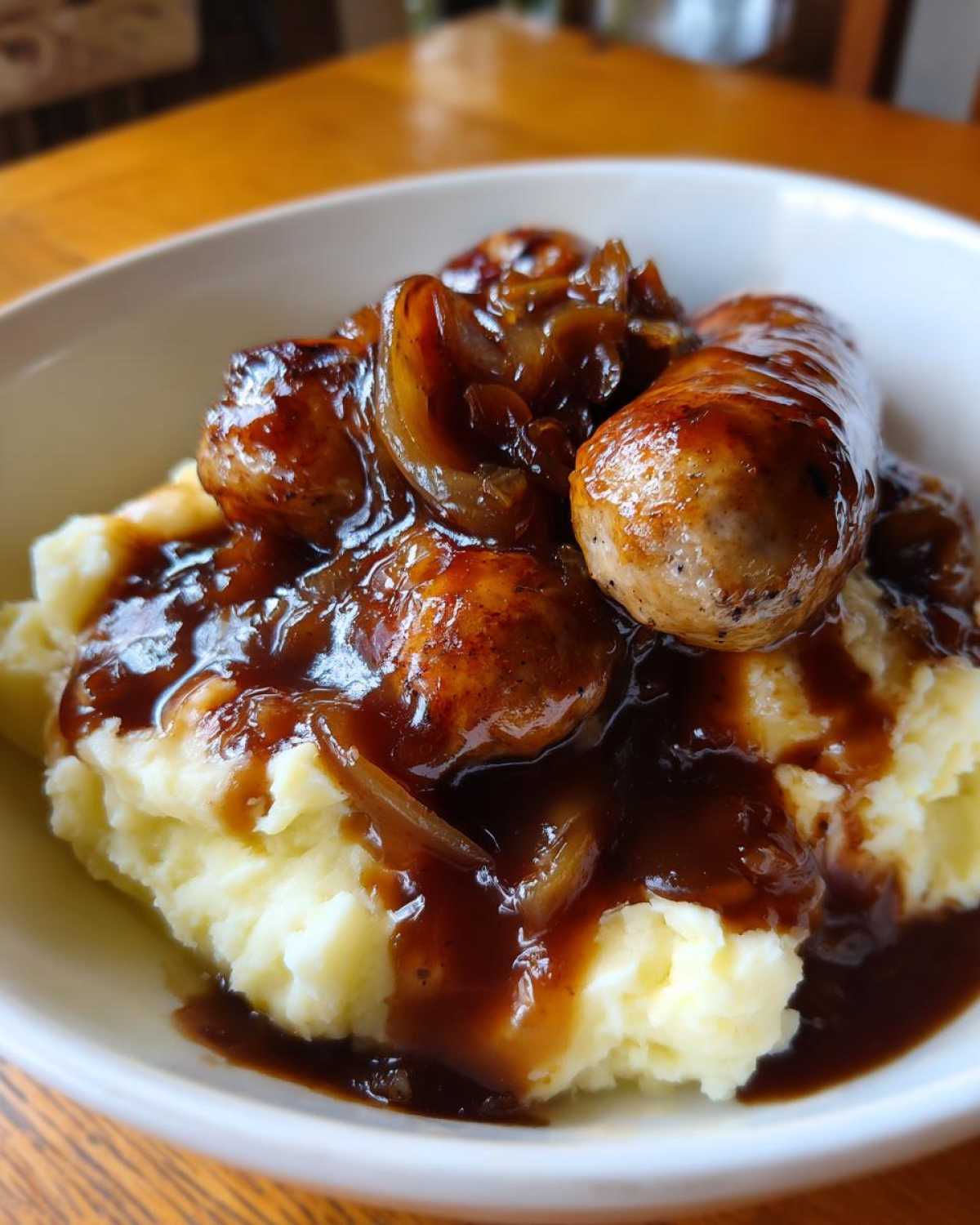Close-up of a bowl of bangers and mash topped with caramelized onions and dark gravy.