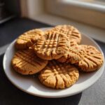 A stack of golden brown peanut butter cookies with classic crosshatch fork marks, sitting on a white plate.