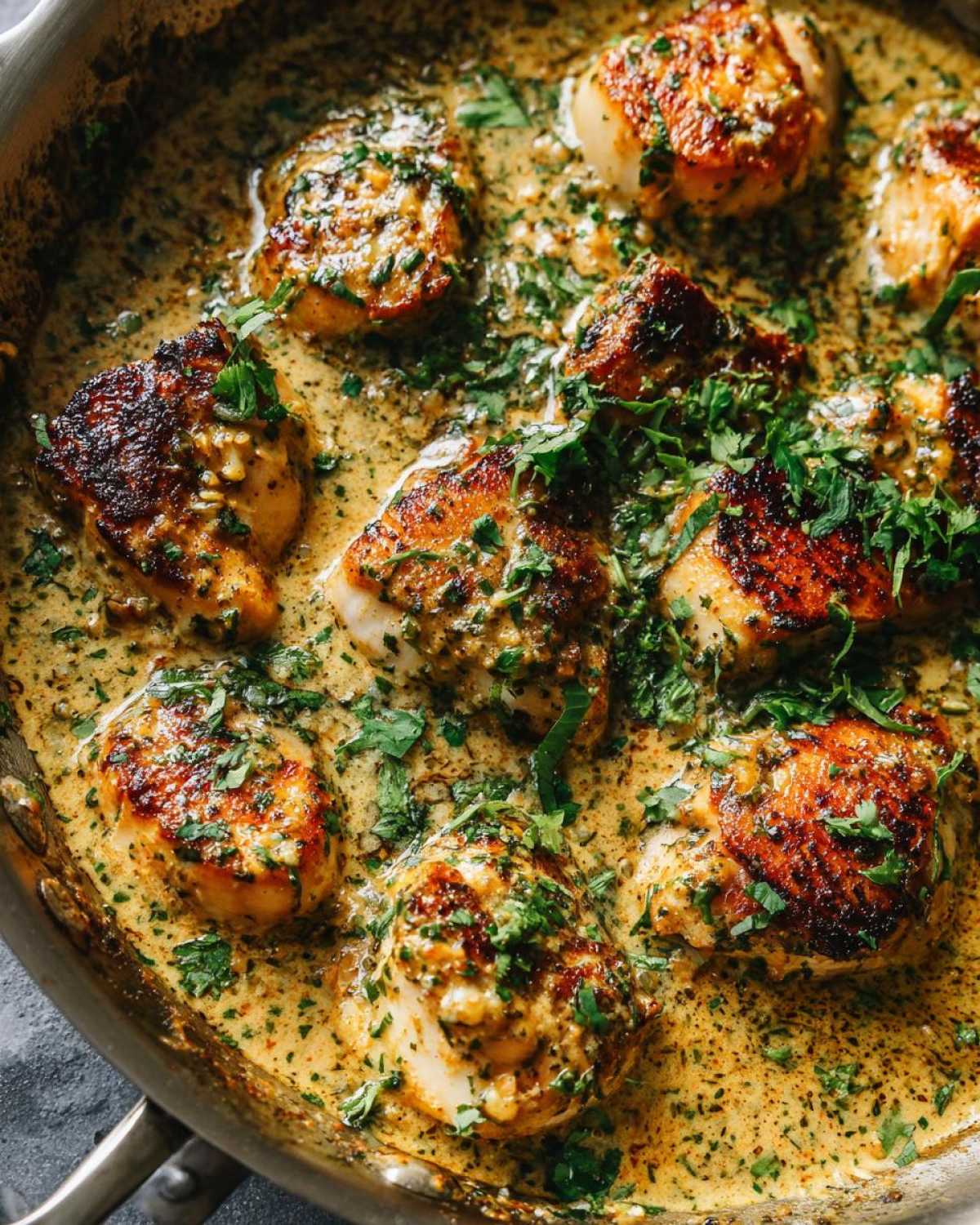 Close-up of seared coconut lime chicken pieces simmering in a rich, creamy, herb-flecked sauce in a skillet.