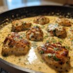 Close-up of seared chicken pieces simmering in a rich, creamy coconut lime chicken sauce garnished with fresh herbs.