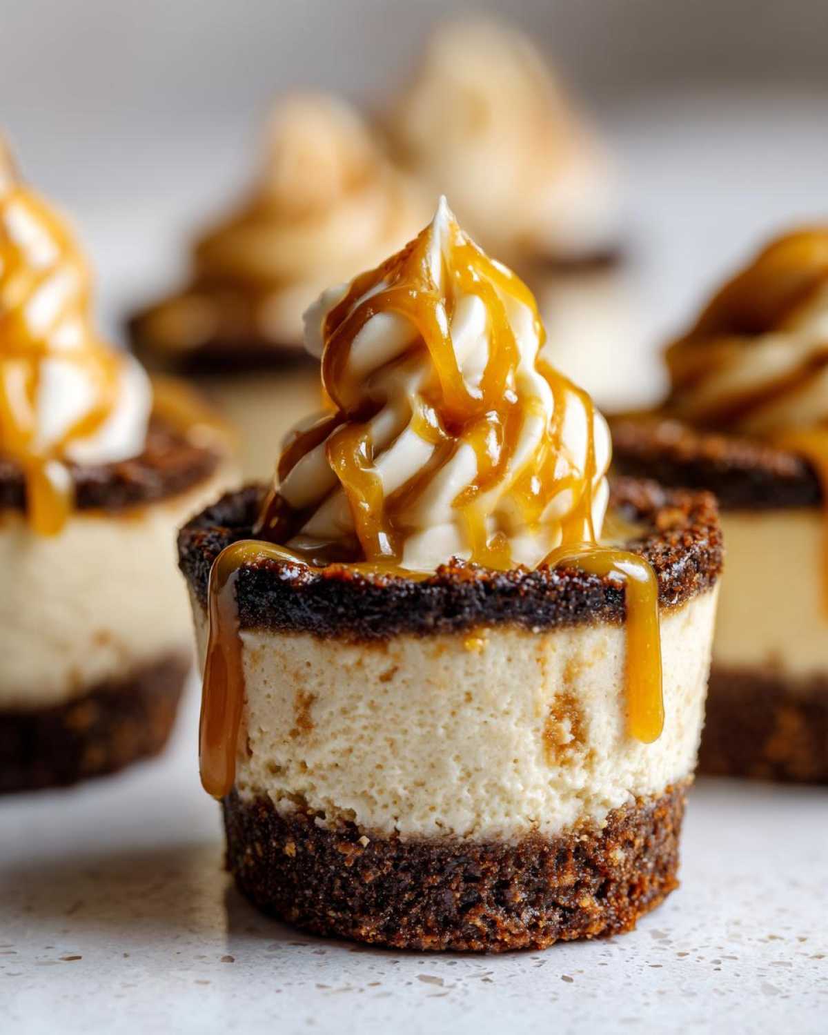 A close-up of one of the finished cookie butter cheesecake cups, topped with whipped cream and drizzled heavily with caramel sauce.