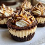 Close-up of a single cookie butter cheesecake cup with a dark crust, creamy filling, and whipped topping drizzled with caramel and chocolate.