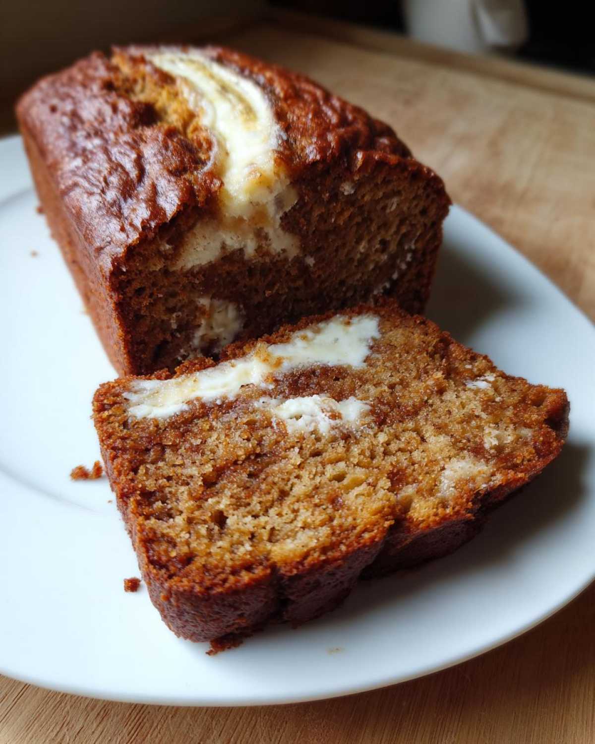 A slice cut from a loaf of rich, brown cream cheese banana bread, showing the creamy white swirl inside.