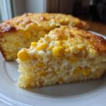 A close-up of a slice of moist cream cheese corn casserole showing whole corn kernels embedded in the yellow base.