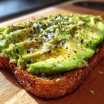 Close-up of creamy avocado toast topped with flaky sea salt and cracked black pepper.