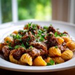 A close-up shot of rich, saucy creamy beef pasta served on a white plate, garnished with fresh parsley.