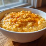 A close-up shot of a white bowl filled with creamy cheese grits topped with melted cheddar cheese.