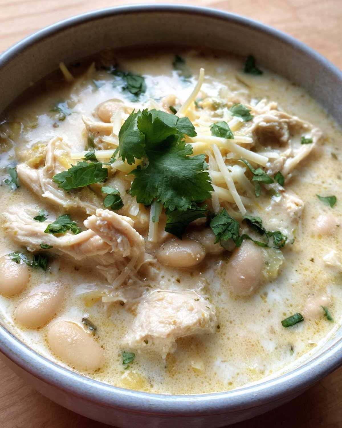 Close-up of a creamy white chicken chili topped with shredded cheese, white beans, and fresh cilantro.