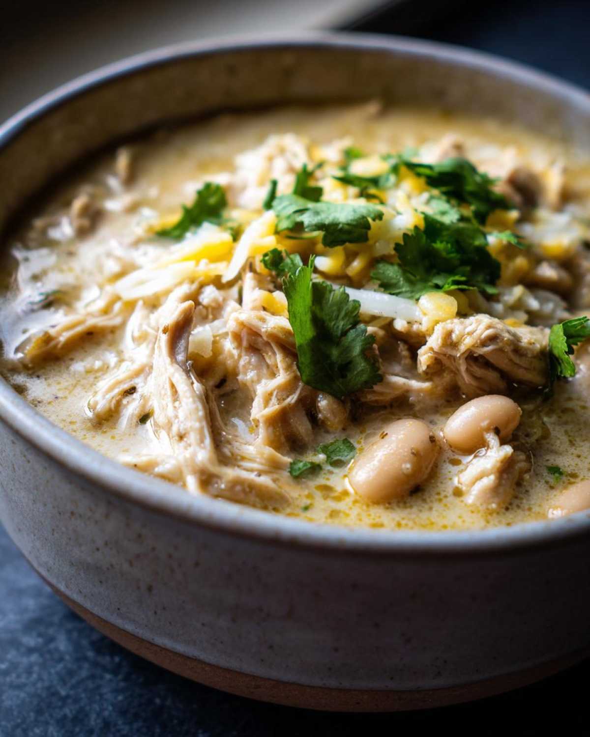 Close-up of creamy white chicken chili topped with shredded cheese, cilantro, and white beans.