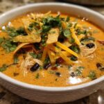 Close-up of a bowl of creamy chicken tortilla soup topped with shredded cheese, tortilla strips, and cilantro.