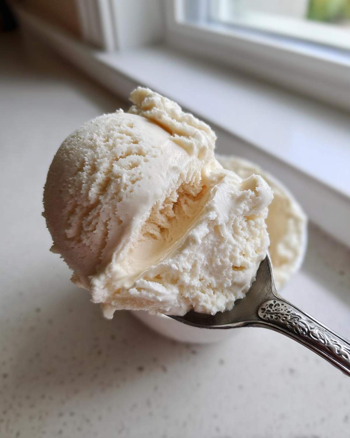 A close-up shot of a perfectly scooped portion of creamy white cottage cheese ice cream being lifted on an ornate silver spoon.