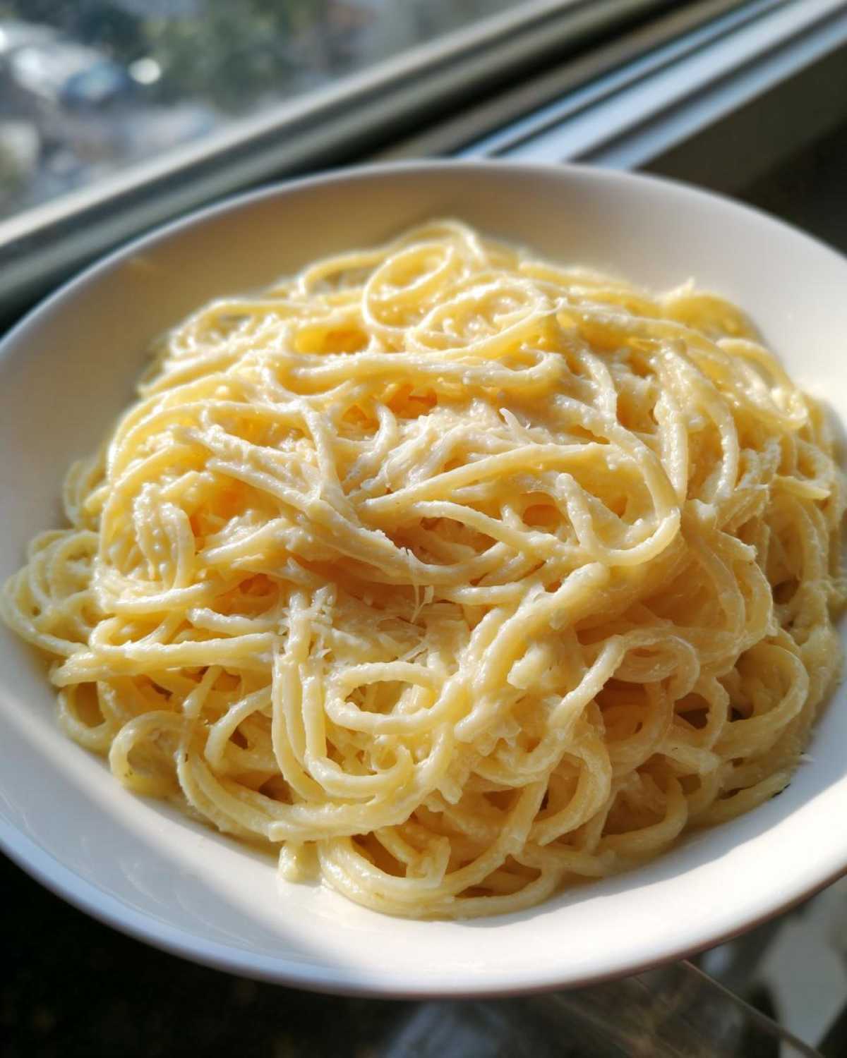A close-up of creamy spaghetti coated in a rich garlic parmesan sauce, served in a white bowl.