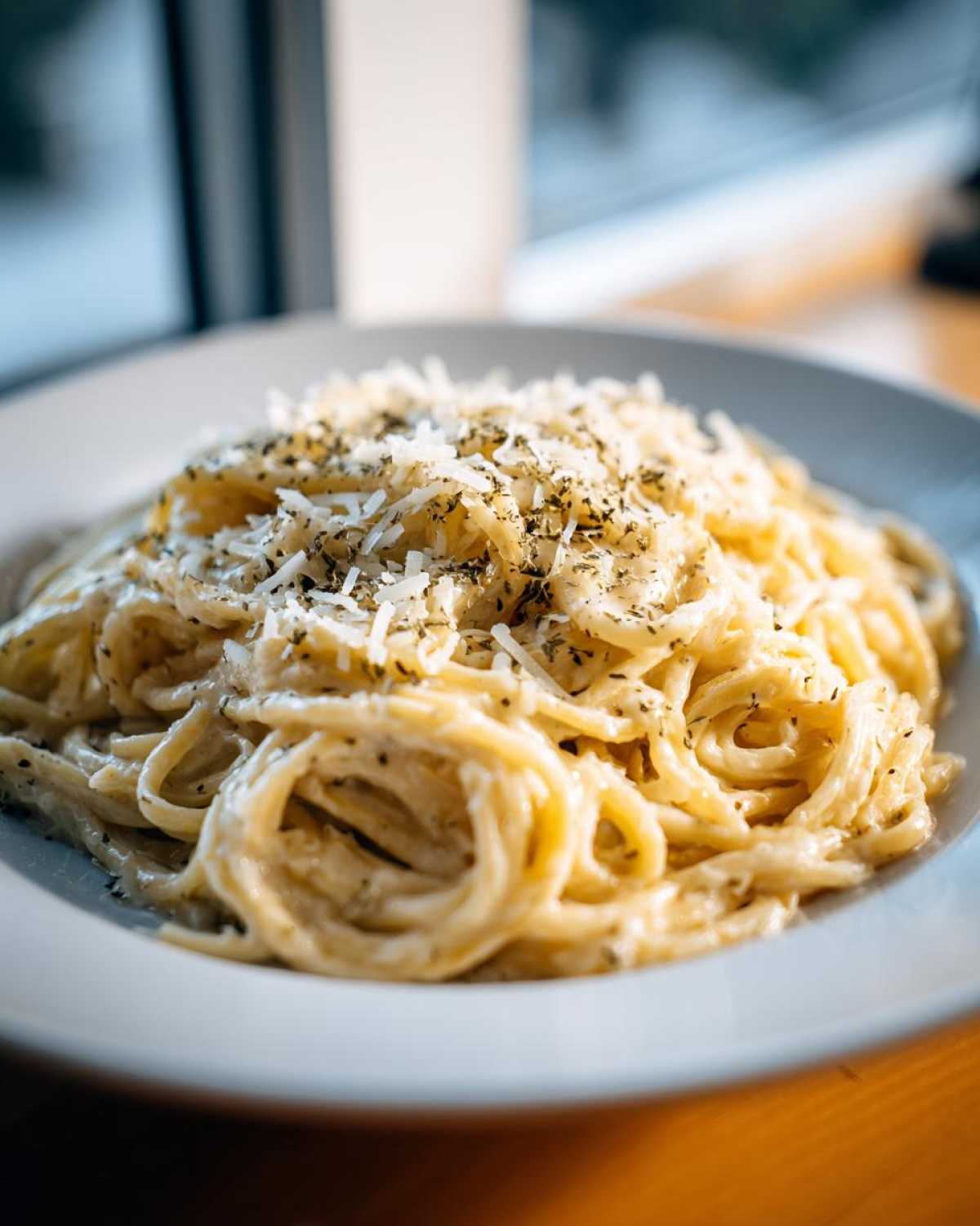 Close-up of creamy spaghetti tossed in a sauce, topped generously with shredded cheese and herbs, representing a quick garlic parmesan pasta.