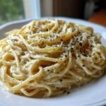 Close-up of creamy spaghetti tossed in a rich sauce, topped with grated cheese and black pepper, representing garlic parmesan pasta.