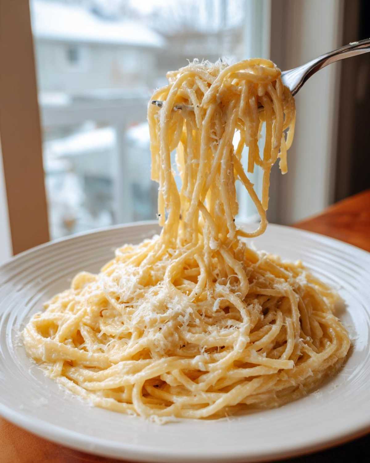A fork lifting a generous portion of creamy garlic parmesan pasta from a white plate.