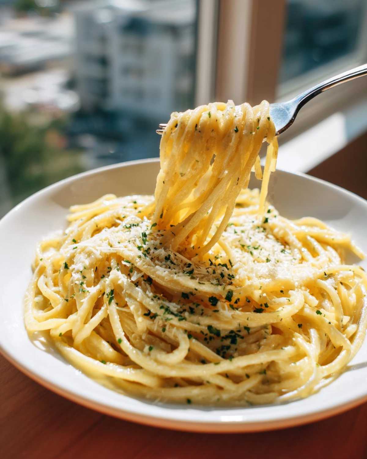 A fork lifting a twirl of creamy garlic parmesan pasta from a white bowl, topped with grated cheese and parsley.