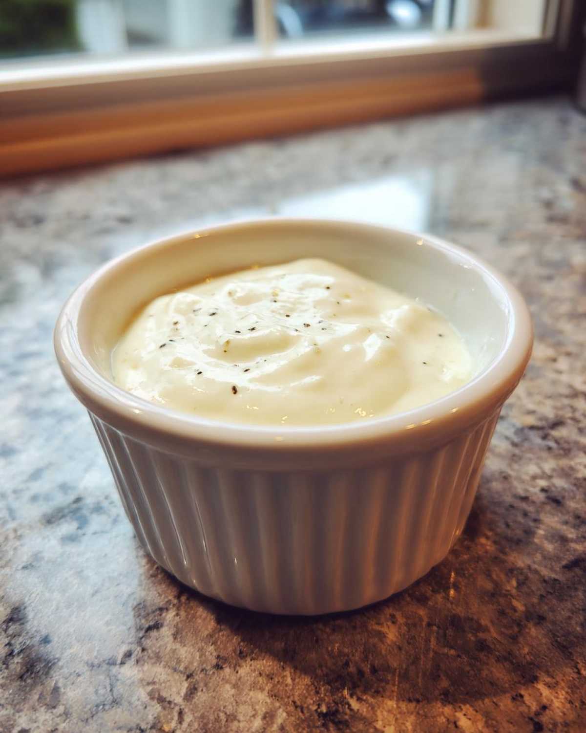 Close-up of creamy, white garlic sauce sprinkled with pepper in a small white ramekin.