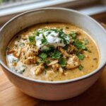 A close-up of creamy keto white chicken chili topped with sour cream and fresh cilantro.