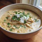 A close-up of a bowl of creamy keto white chicken chili topped with sour cream and fresh cilantro.