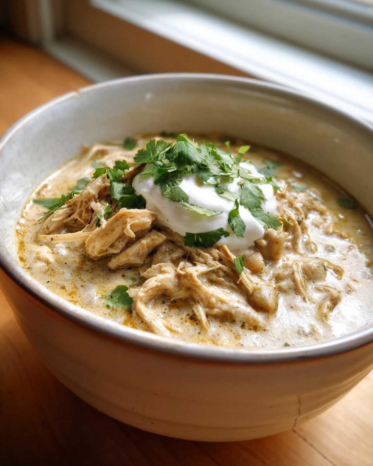 Close-up of creamy keto white chicken chili topped with sour cream and fresh cilantro.