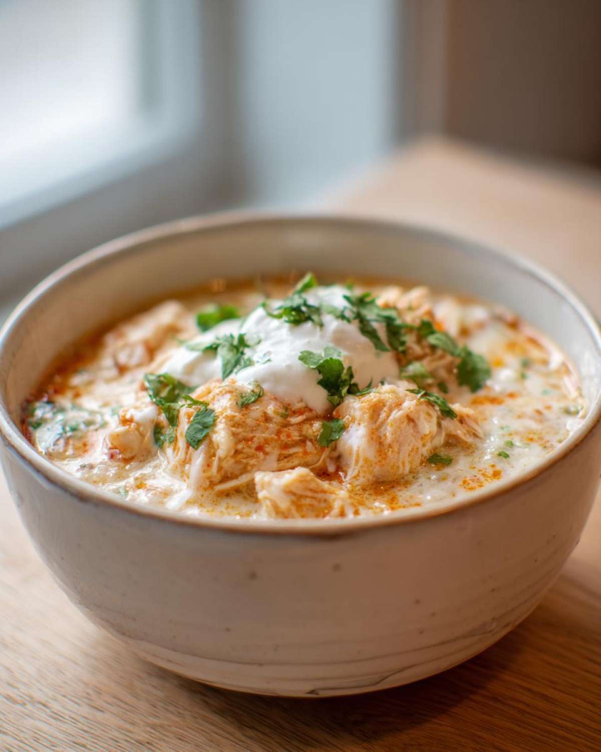 A close-up of a bowl of creamy keto white chicken chili topped with sour cream and fresh cilantro.