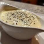 Close-up of creamy peppercorn sauce topped with cracked black and white peppercorns, served in a white gravy boat.