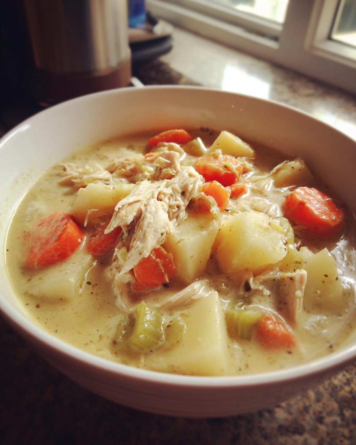 Close-up of a white bowl filled with creamy slow cooker chicken stew, featuring shredded chicken, potatoes, and carrots.