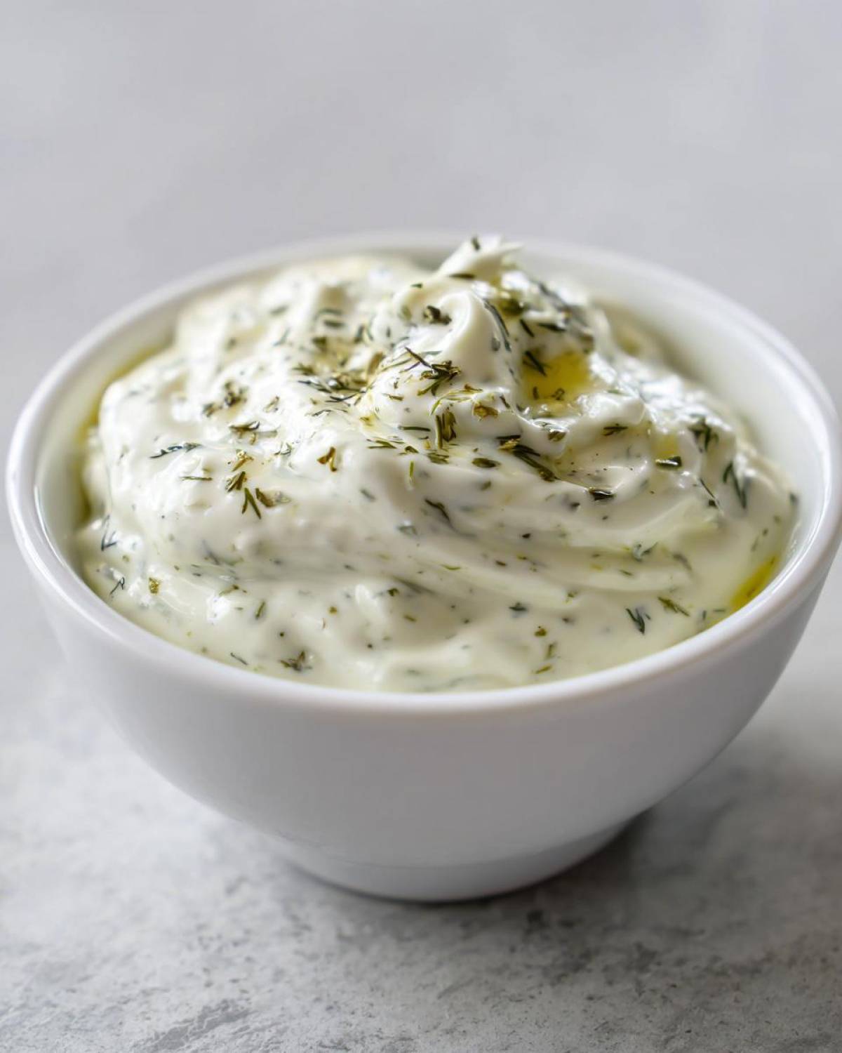 Close-up of creamy, homemade tartar sauce topped with fresh dill in a small white bowl.