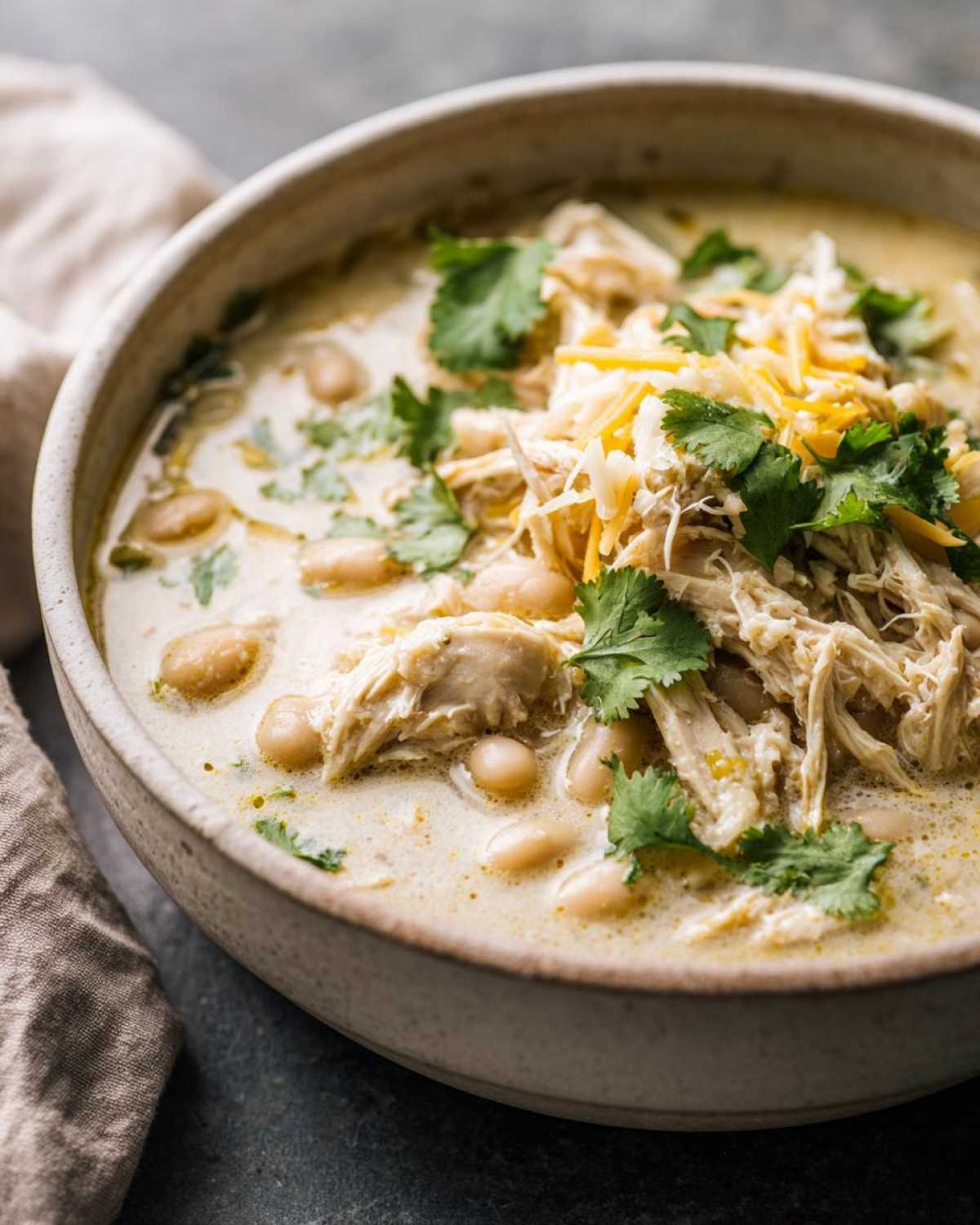 Close-up of a hearty bowl of creamy white chicken chili topped with shredded cheese and fresh cilantro.