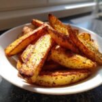 A close-up of golden brown, seasoned air fryer potato wedges piled high in a white bowl.