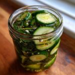 Close-up of sliced cucumbers and fresh dill submerged in brine for homemade refrigerator pickles.