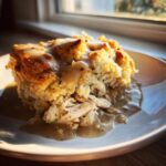 A close-up serving of moist crock pot chicken and stuffing topped with savory gravy on a white plate.