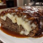 Close-up of a slice of crockpot french onion meatloaf topped with melted white cheese and rich brown gravy.