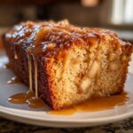 Close-up of a slice of moist apple dapple cake topped with rich caramel sauce dripping down the side.