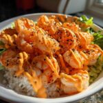 Close-up of a vibrant shrimp bowl featuring seasoned shrimp drizzled with orange sauce over rice and lettuce.