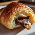Close-up of a flaky, golden brown chocolate croissant with rich, melted chocolate oozing out.