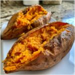 Two perfectly cooked baked sweet potatoes, split open to show the fluffy, bright orange interior seasoned with herbs.