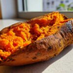 Close-up of a perfectly baked sweet potatoes split open, revealing fluffy, bright orange flesh.