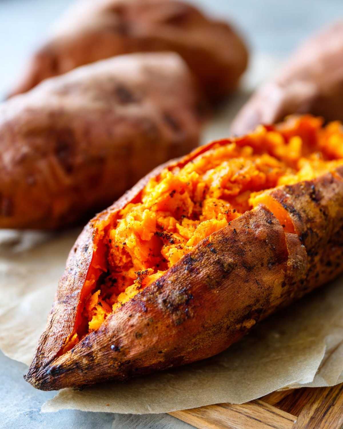 Close-up of a perfectly baked sweet potato split open, revealing fluffy, bright orange flesh seasoned with pepper.