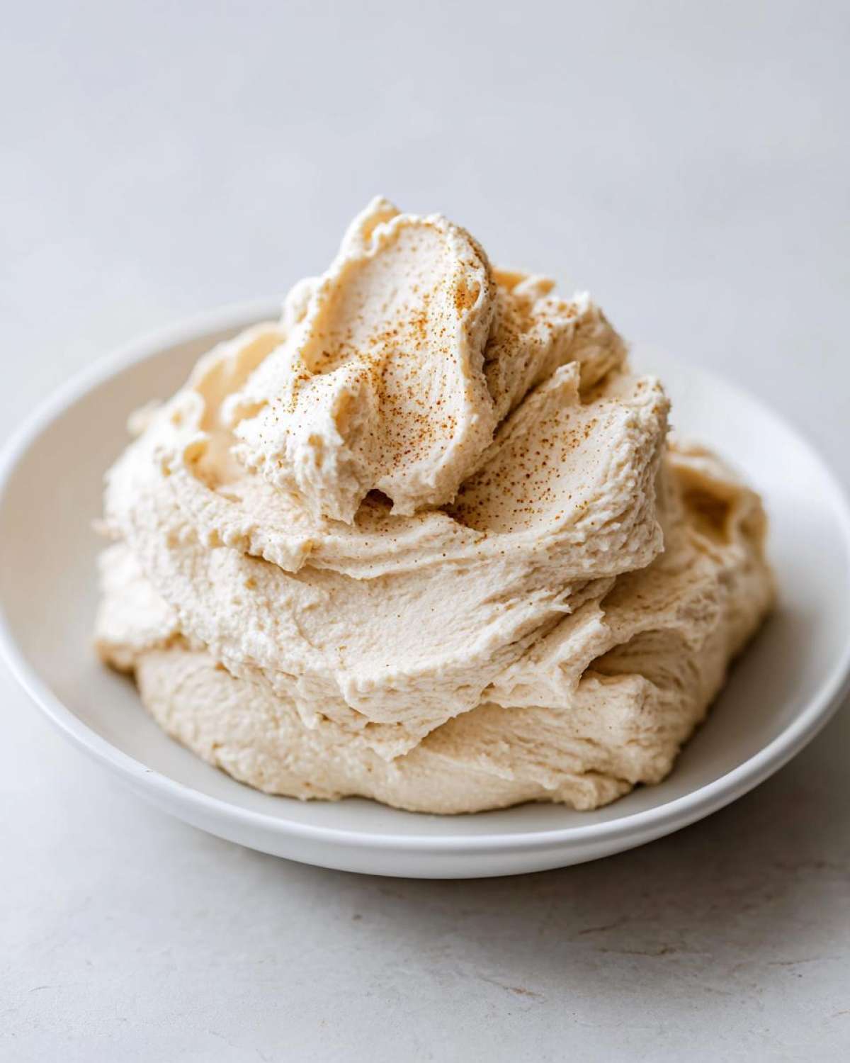 A generous serving of fluffy, whipped cinnamon butter sprinkled with spice in a white bowl.