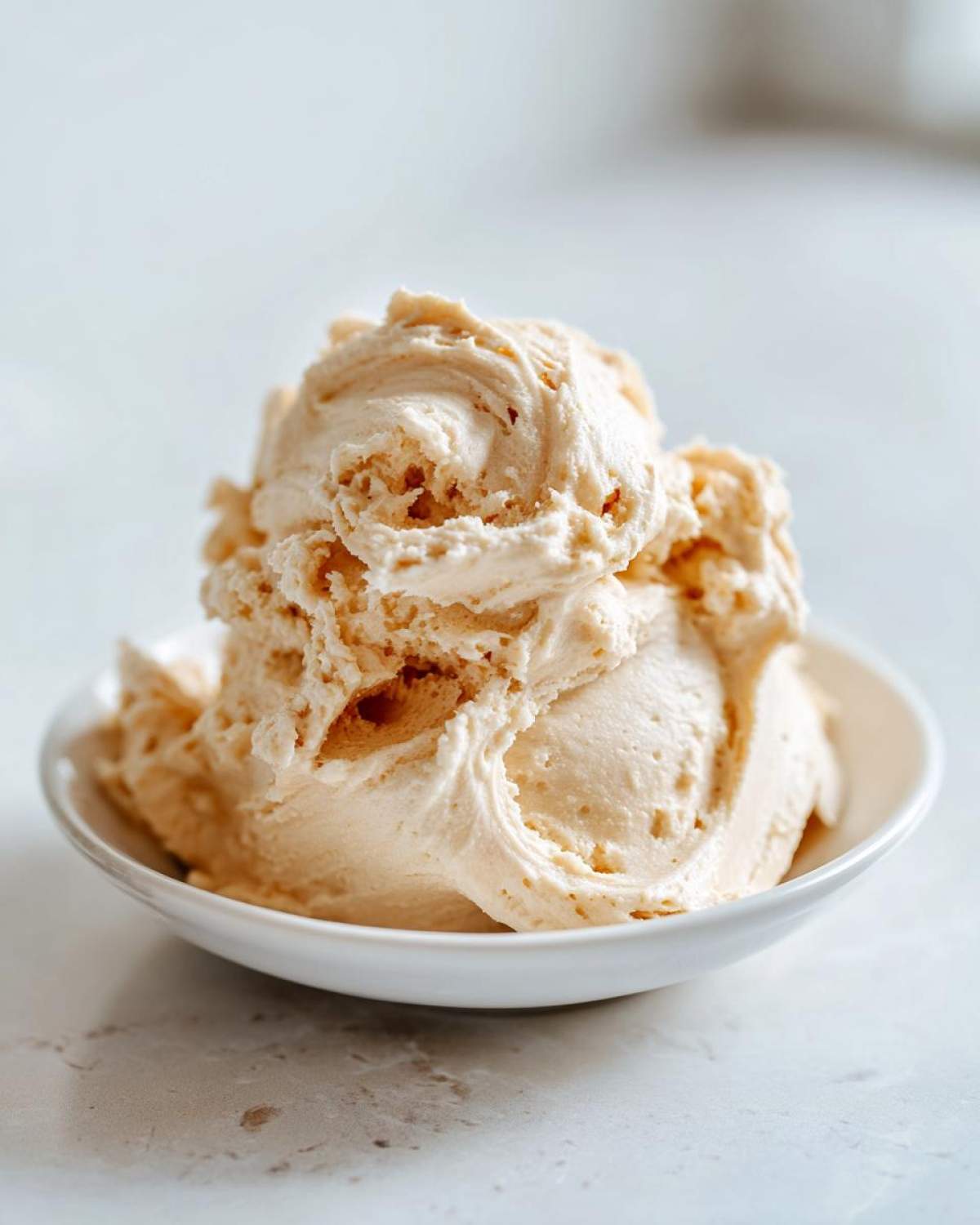 A generous scoop of light brown, fluffy cinnamon butter served in a small white bowl.