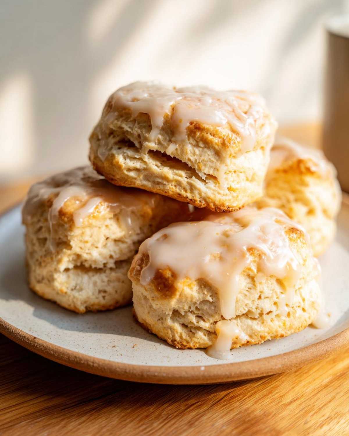 A stack of fluffy, golden lemon scones topped with a thick, dripping lemon glaze, served on a speckled plate.