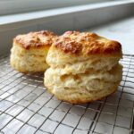 Two tall, fluffy scones with golden-brown tops cooling on a wire rack.