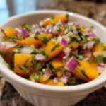 Close-up of vibrant peach salsa featuring diced orange peaches, red onion, and cilantro in a white bowl.