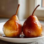 Two glistening, caramelized baked pears sitting in a pool of rich syrup on a white plate.